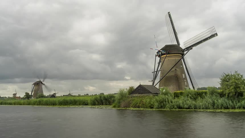 Time lapse of windmill spinning in front of a river on an overcast day