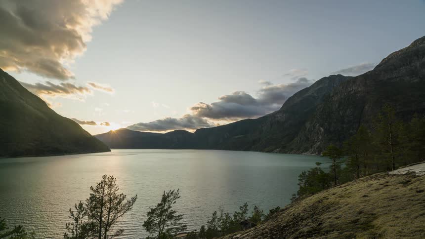 Sunlight peeks through dense clouds moving over a lake
