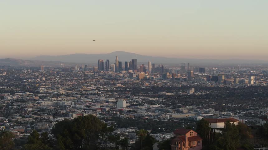 Aerial tracking shot of downtown Los Angeles skyline in the distance and Hollywood Hills in the foreground