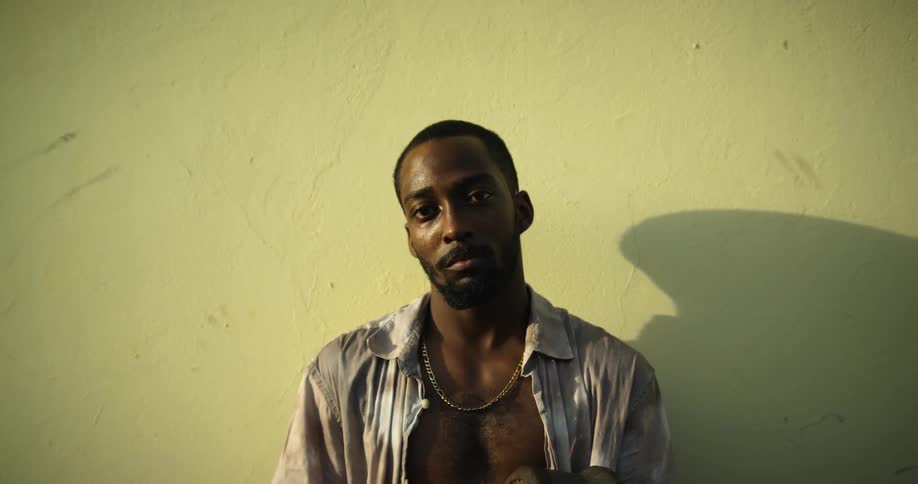 Man with open shirt poses against wallcasting shadow onto surface