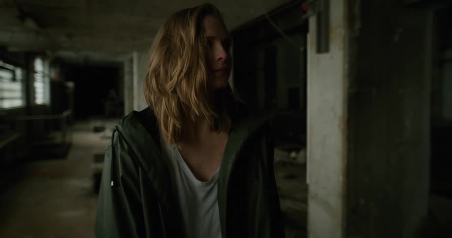 Young blonde woman wearing a green jacket walking inside an abandoned building