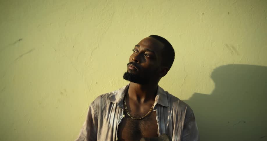 A man with a necklace standing by a wall