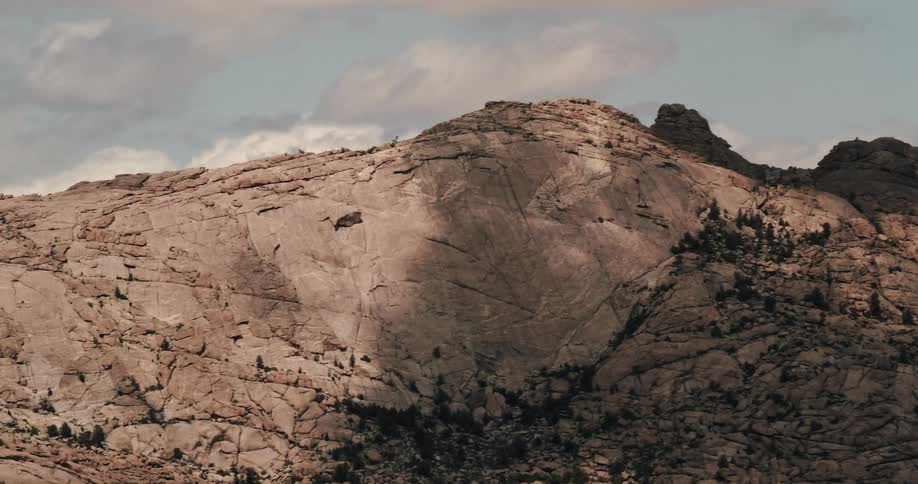 Shadows cover portion of craggy mountain dotted with vegetation as it stand under cloudy sky