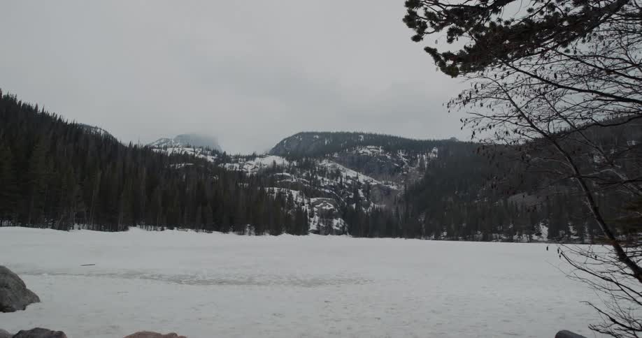View of snowy field with distant forest on mountain slope under clouds