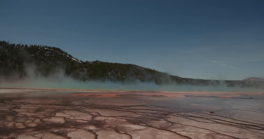 A colorful geyser with smoke/steam with hill and sky