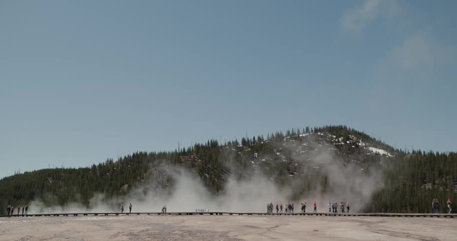 People walking and standing with a hill smoke trees the sky and clouds in the background
