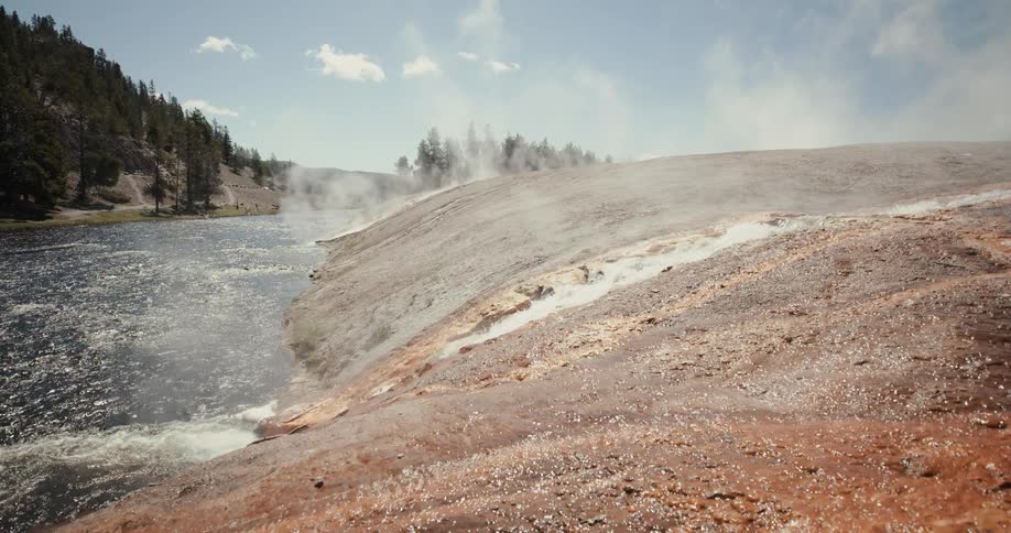 Hot spring streams surrounded by mist flowing into a river near the pine tree forest