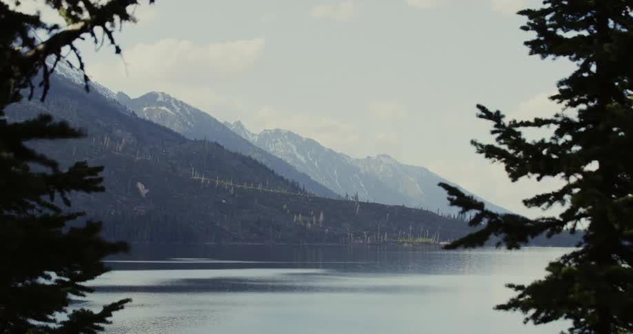 A lake surrounded by trees and mountains in the wilderness on a cloudy day