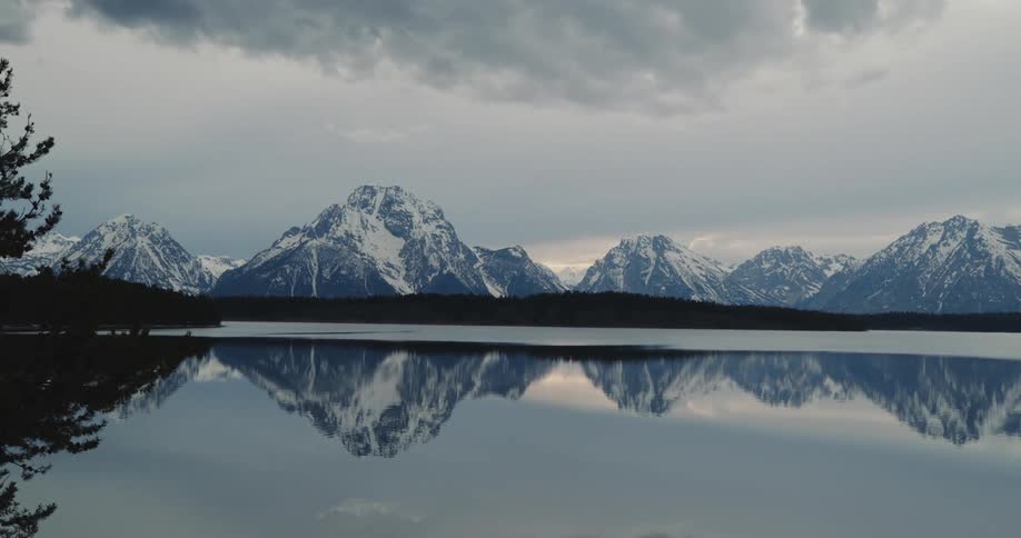 A placid lake reflects the snow capped mountains and sky