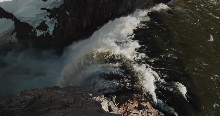 Aerial view of clear water river flowing into a waterfall in the mountains