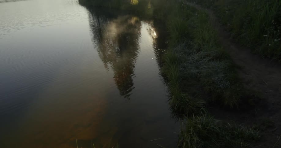 Dirt path parallels rippling water that reflect bright sun and trees