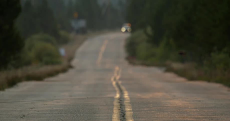A vehicle drives down a street in a rural area and turns towards a building