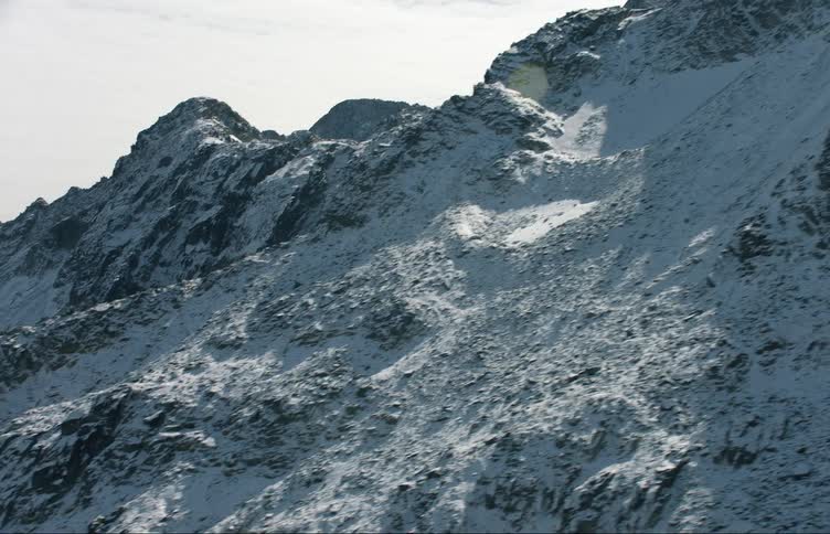 A lake surrounded by snow covered mountains with peaks high in a cloudy sky
