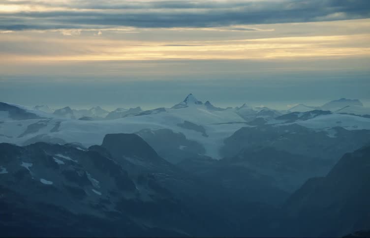 Aerial view of snow on the slopes of a large mountain range at sunset