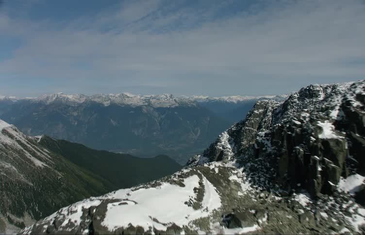 A mountain range covered in snow and ice with the sky and clouds in the background