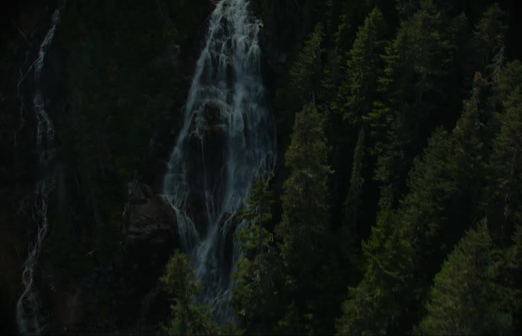 A waterfall and river surrounded by trees with a mountain range the sky and clouds in the background
