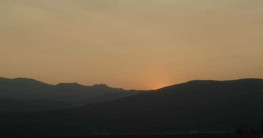 The sun has set over mountains in an orange sky
