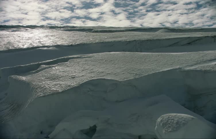 Snow and ice cover land under cloudy sky