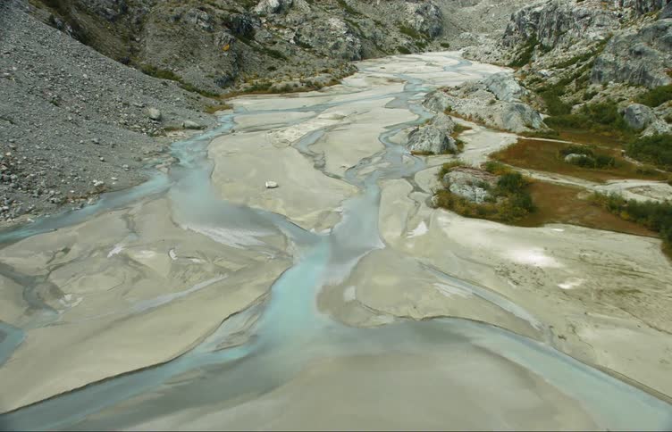 Camera is flying over the river that flows through the rocky canyon