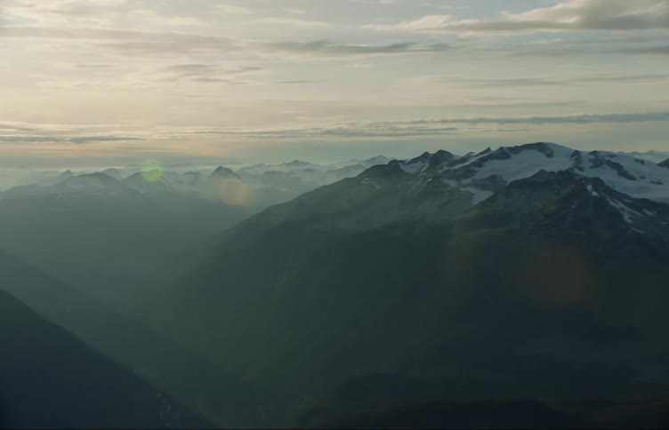 Aerial view of the snow covered peaks of a mountain range in the mist at sunset