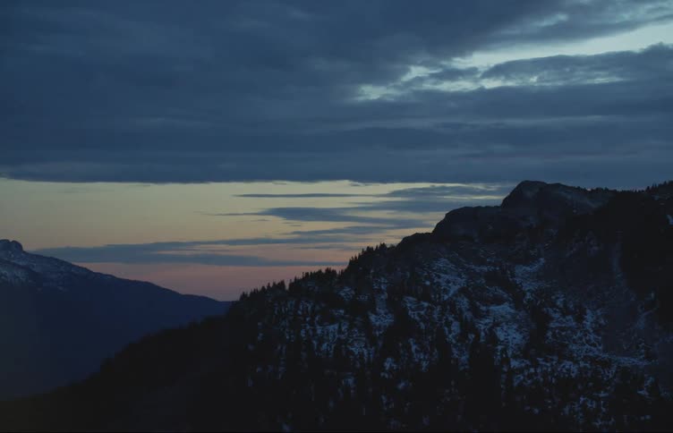 Sunset causes a golden sky beneath gray clouds behind a mountain range