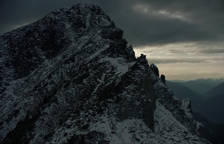 A mountain range covered in snow and ice with the sky and clouds in the background