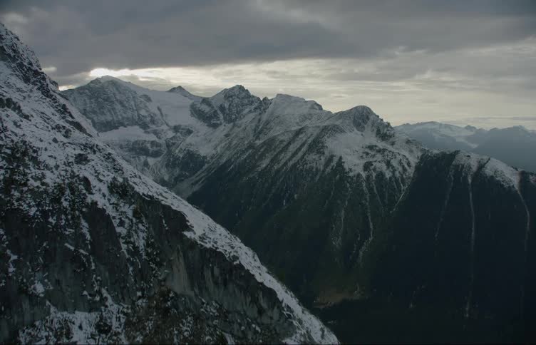 A mountain range covered in snow and ice with the sky and clouds in the background