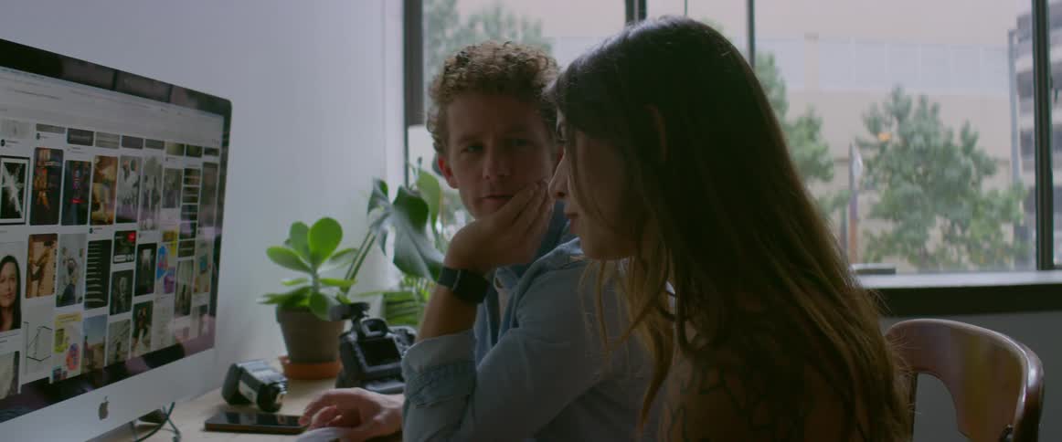 Man and woman sit at desk using desktop computer in studio