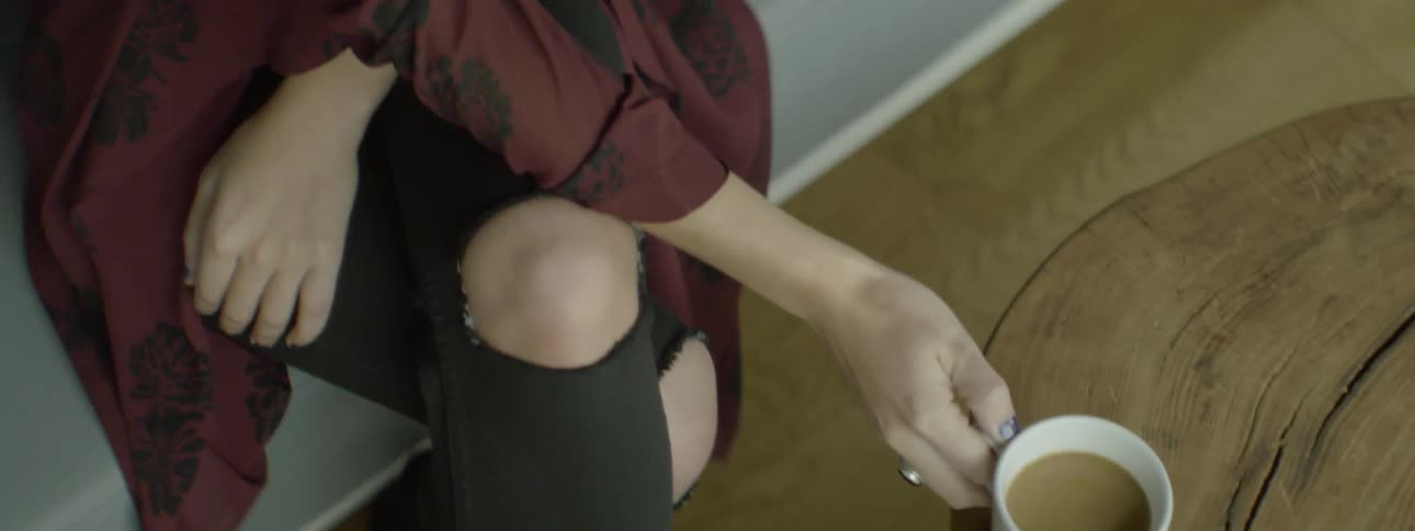 A woman picks up a coffee cup and takes a sip
