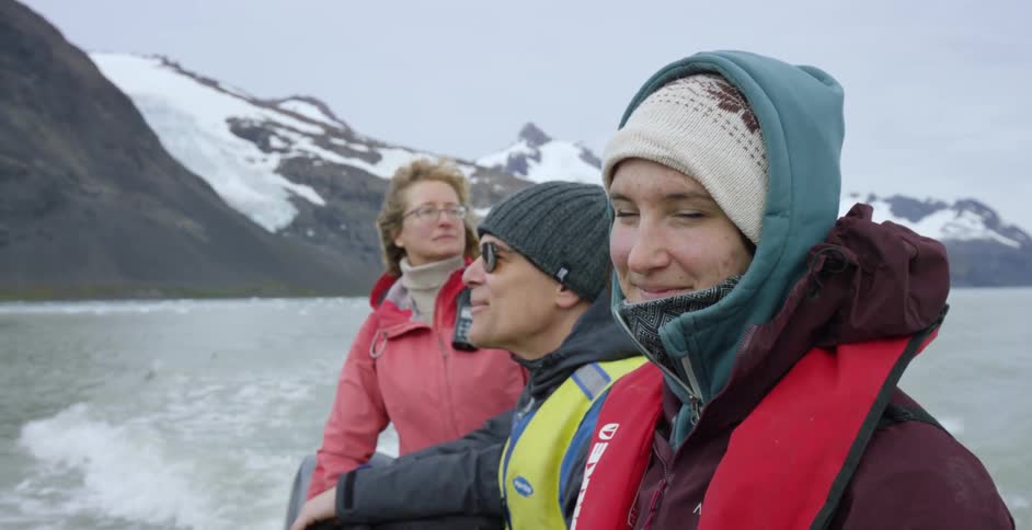 People look at snow covered mountains from a moving boat