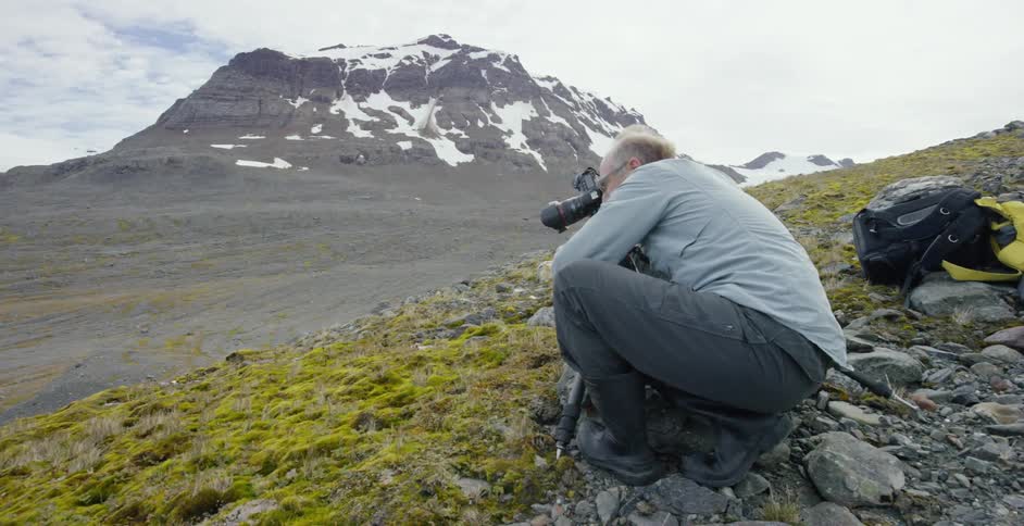 A man is crouched taking photographs on a mountain range