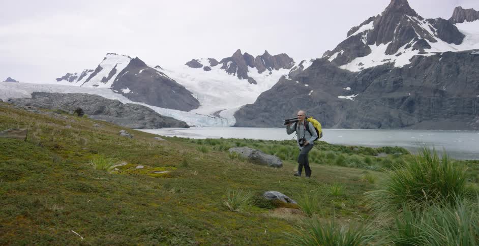 A man is walking uphill carrying a tripod