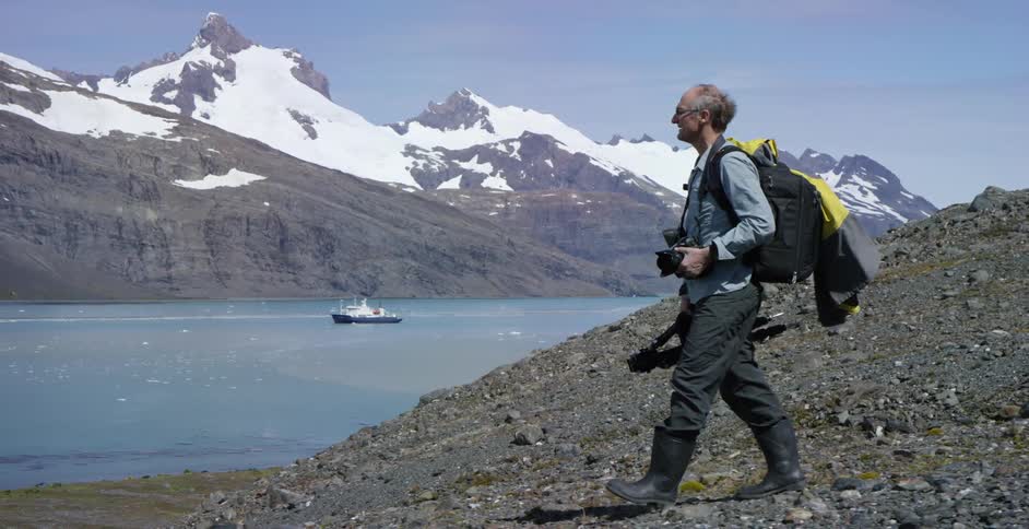 A photographer walks down a rocky slope toward a mountain lake