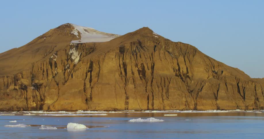 Icebergs float beside a large barren rock formation