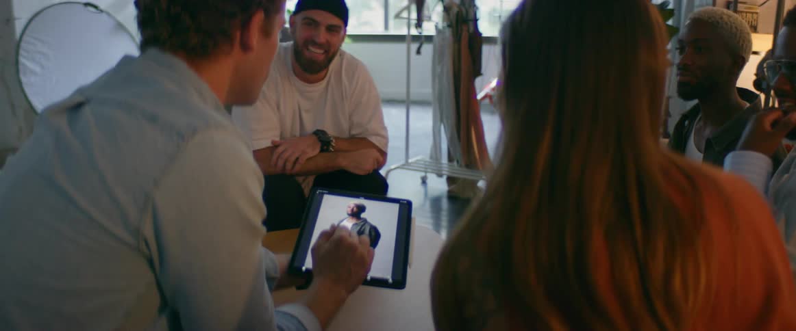 Group of models gather around a photographer to check pictures on a tablet