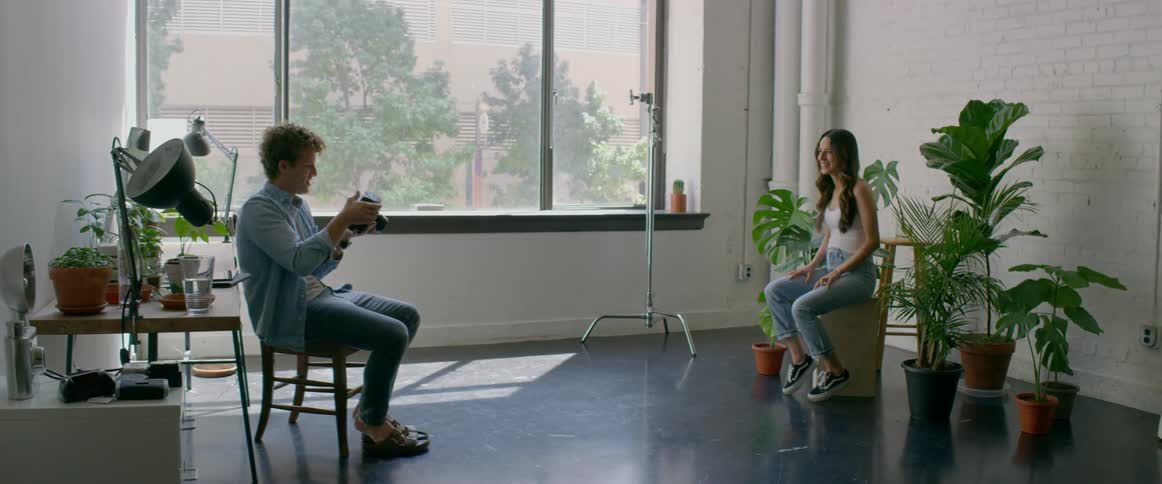 A man in a room with a camera taking a picture of a woman with a wall in the background