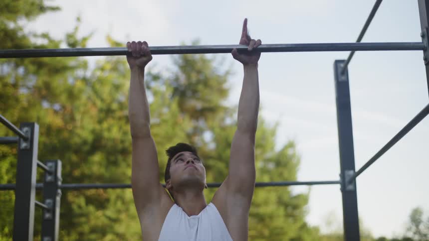 A man is doing pull ups in the park