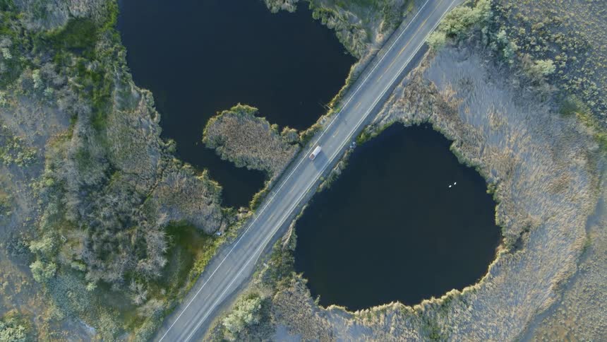 A truck travels on a rural highway between two wetland ponds