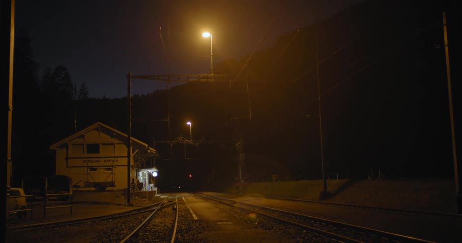 Train tracks pass forest train station and parking lot at night