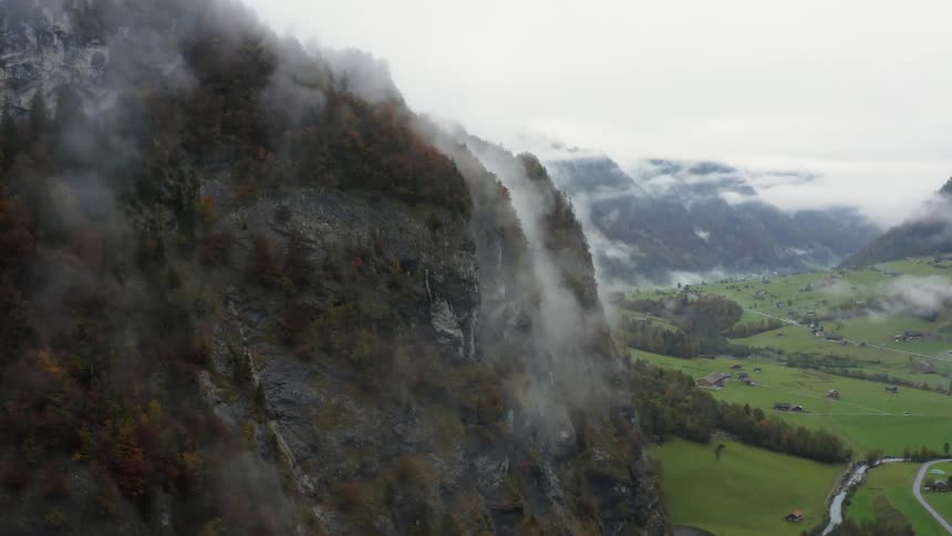 Low lying clouds obscure tops of mountains surrounding green valley with road and river winding through it