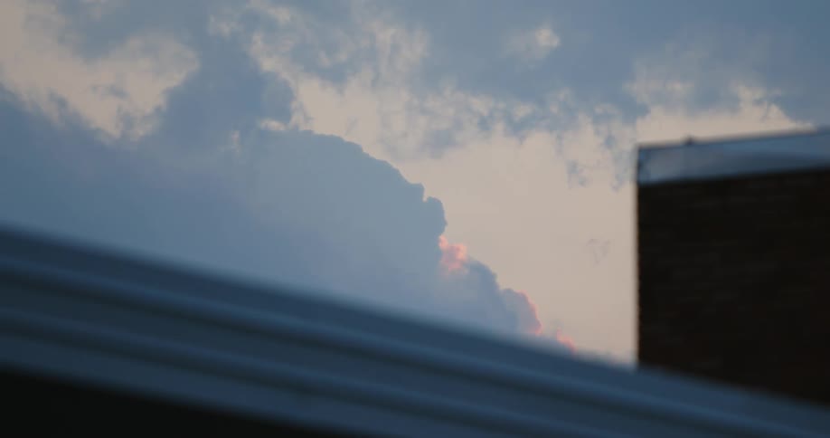 Darker clouds move across sky over building obscuring red tinted clouds