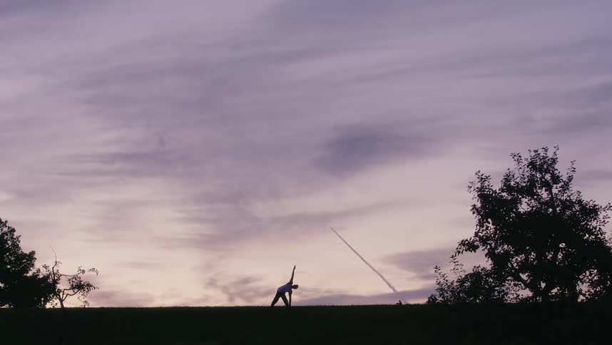 Man moves through yoga poses under cloudy sky on lawn