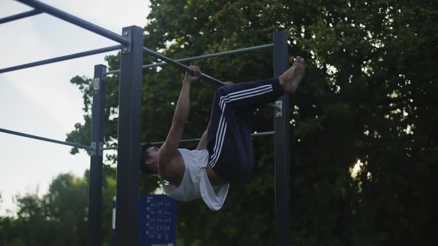 A man is doing pull ups in the park