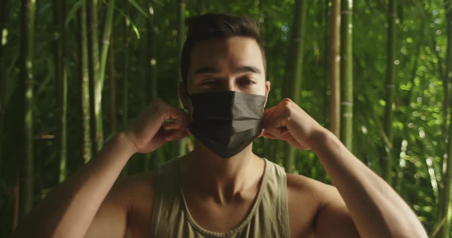 Young man standing in front of a bamboo forest takes off a black face mask