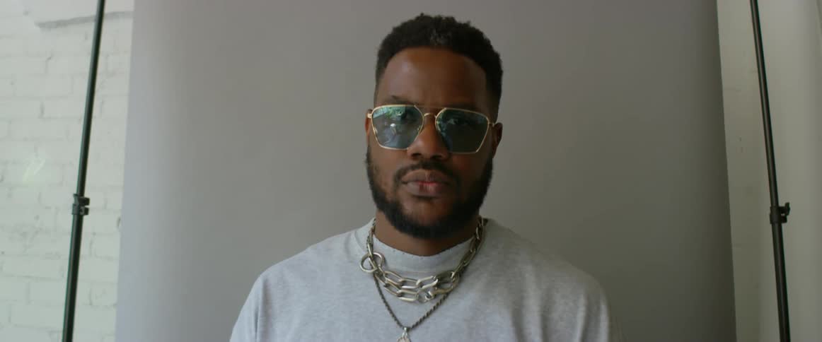 Male model with sunglasses beard chain necklace and gray sweatshirt looks at the camera in the studio
