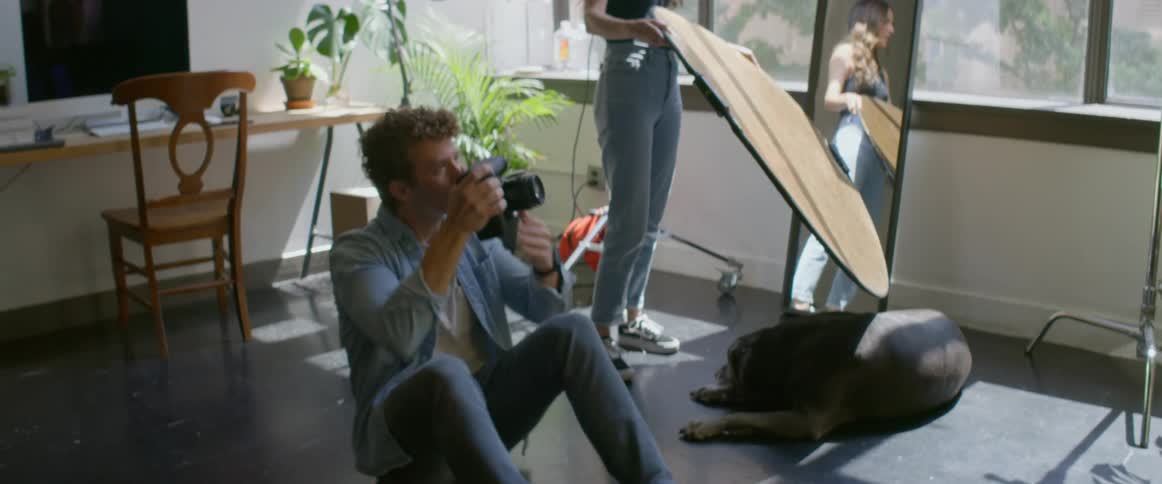 A woman holds a board above a dog as a man moves around and takes photos