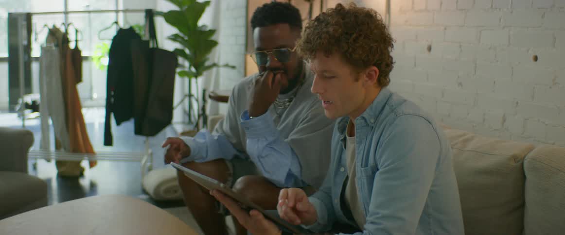 Two men sitting on a couch inside a studio looking at pictures on a tablet
