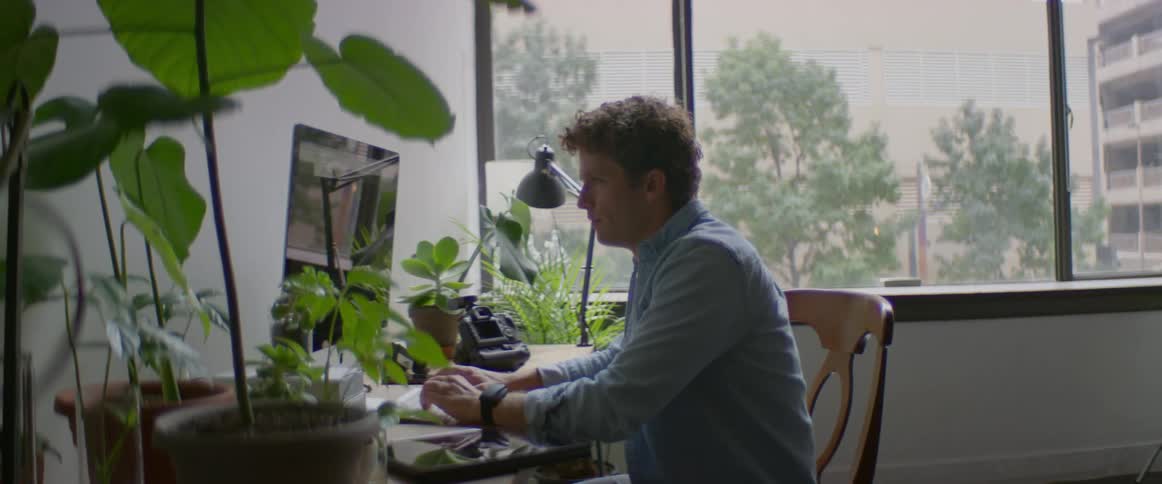 Man sits at desk using computer with camera on table nearby