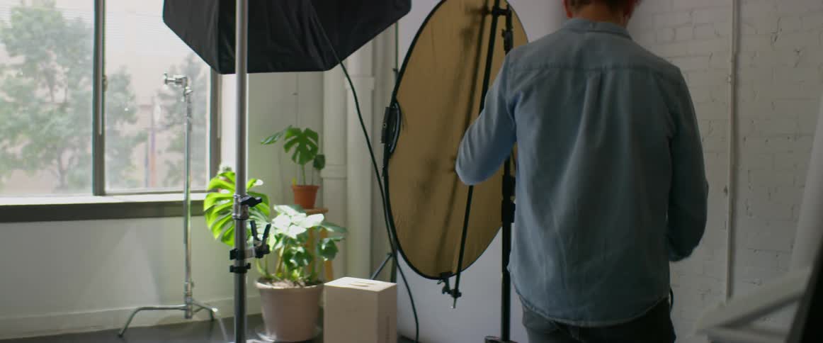 A man in a room plugging in a spotlight with a wall and window in the background