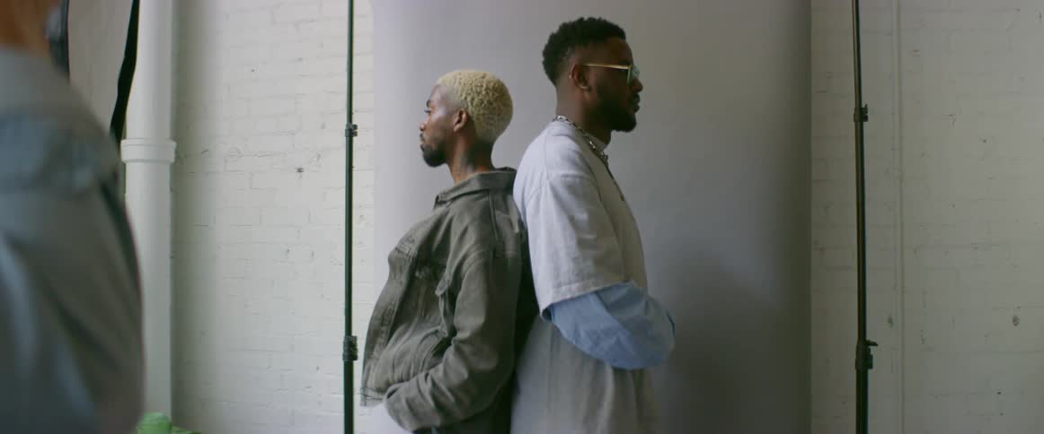 Photographer takes pictures of two male models standing back to back in photography studio